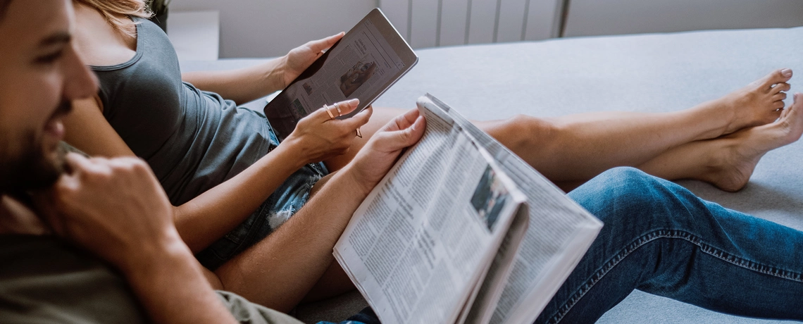 Paar liest Nachrichten in der Zeitung und auf einem Tablet