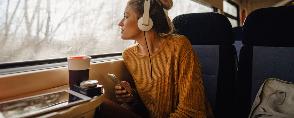 Frau sitzt im Zug und hört Nachrichten mit ihrem Handy über Kopfhörer